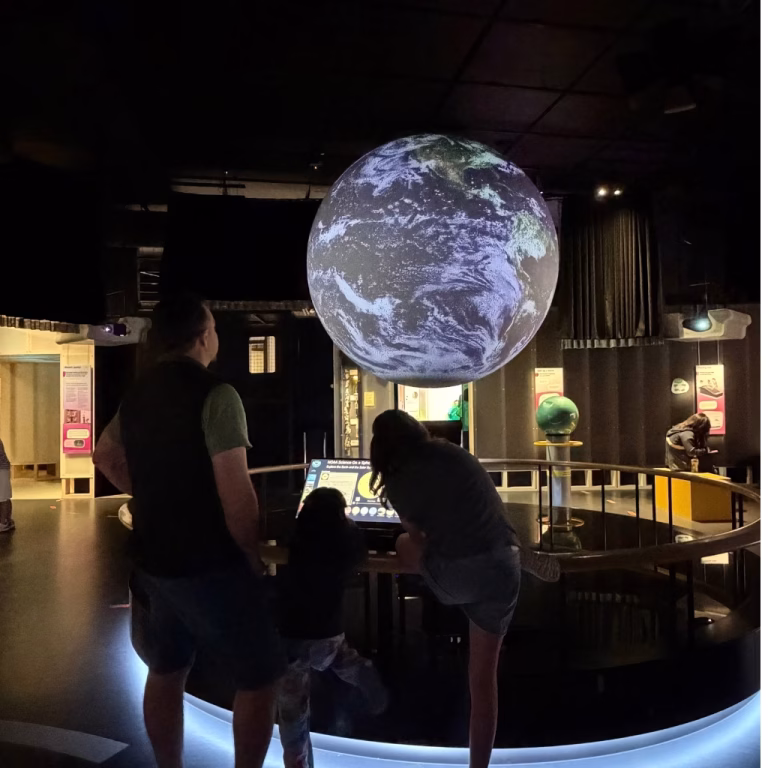 Murray with his daughter and her cousin looking at the rotating globe on Science on a Sphere at SparkLab