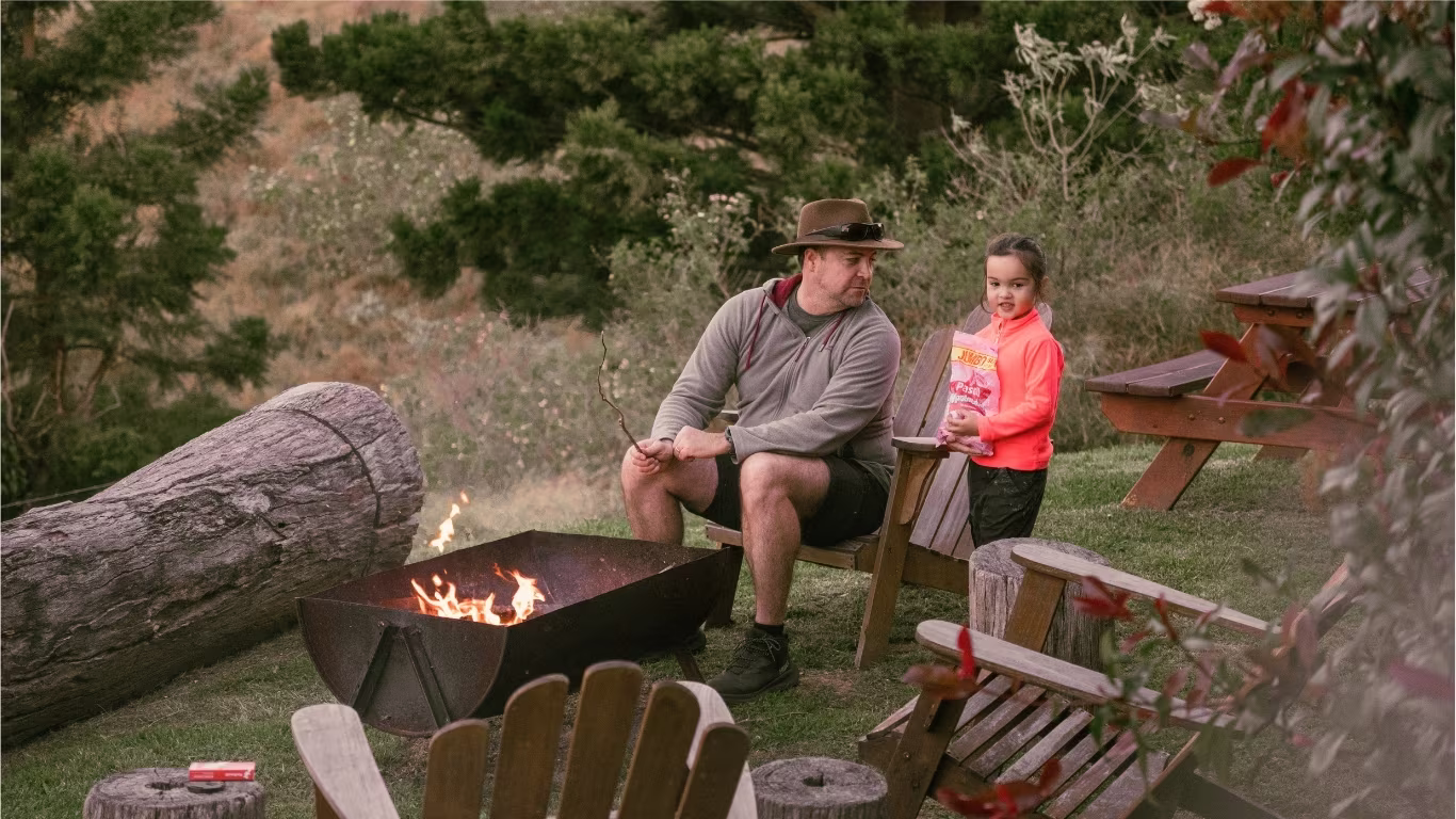 Father and daughter roasting marshmallows over the outdoor fire pit at Worendo Cottages, a Scenic Rim farm stay
